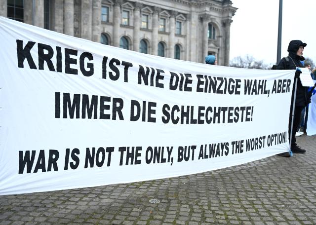 05 December 2025, Berlin: Demonstrators stand in front of the German Bundestag holding a banner reading 'War is never the only choice, but always the worst!'. Photo: Elisa Schu/dpa