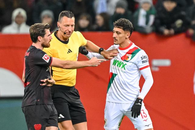 06 December 2025, Bavaria, Augsburg: Referee Sven Jablonski seperates Bayer Leverkusen's Jonas Hofmann and Augsburg's Dimitris Giannoulis during the German Bundesliga soccer match between FC Augsburg and Bayer Leverkusen at the WWK-Arena. Photo: Harry Langer/dpa - IMPORTANT NOTICE: DFL and DFB regulations prohibit any use of photographs as image sequences and/or quasi-video.