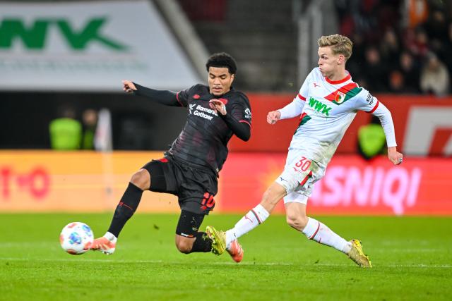 06 December 2025, Bavaria, Augsburg: Bayer Leverkusen's Malik Tillman (L) in action against Augsburg's Anton Kade during the German Bundesliga soccer match between FC Augsburg and Bayer Leverkusen at the WWK-Arena. Photo: Harry Langer/dpa - IMPORTANT NOTICE: DFL and DFB regulations prohibit any use of photographs as image sequences and/or quasi-video.