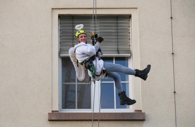 06 December 2025, Saxony, Chemnitz: A member of the Chemnitz fire department's height rescue team abseils down the facade of the hospital in a Christmas angel costume. For the past five years, fire department rescuers have been organizing an abseiling campaign at children's hospitals across Germany on St. Nicholas' Day and delighting patients and staff with small gifts. Photo: Sebastian Willnow/dpa
