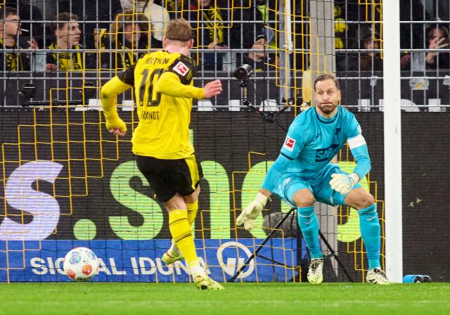 07 December 2025, North Rhine-Westphalia, Dortmund: Borussia Dortmund's Julian Brandt (L) scores his side's first goal against Hoffenheim goalkeeper Oliver Baumann during the German Bundesliga soccer match between Borussia Dortmund and TSG 1899 Hoffenheim at Signal Iduna Park. Photo: Bernd Thissen/dpa - IMPORTANT NOTE: In accordance with the regulations of the DFL German Football League and the DFB German Football Association, it is prohibited to utilize or have utilized photographs taken in the stadium and/or of the match in the form of sequential images and/or video-like photo series.
