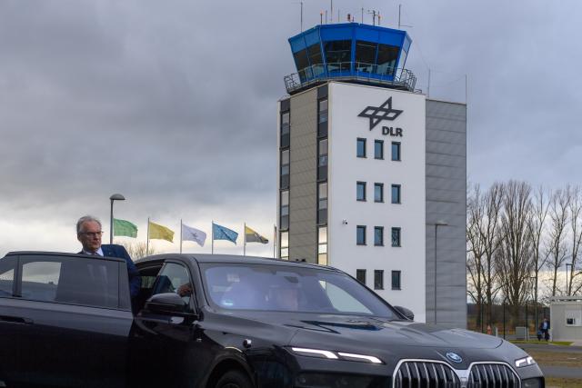 08 December 2025, Saxony-Anhalt, Cochstedt: Minister President of Saxony-Anhalt Reiner Haseloff gets into his official car in front of the tower of the National Test Center for Unmanned Aerial Systems of the German Aerospace Center (DLR). An event was held there at which the DLR provided information about the prospects for drone research. Photo: Klaus-Dietmar Gabbert/dpa