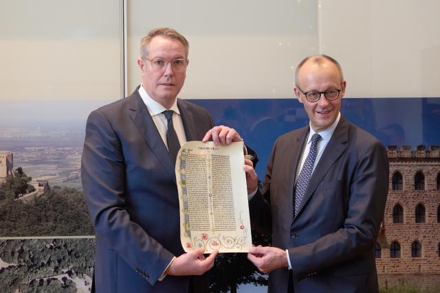 09 December 2025, Rhineland-Palatinate, Mainz: Alexander Schweitzer (L), Minister President of Rhineland-Palatinate, receives German Chancellor Friedrich Merz and presents him with a facsimile of a page from the Gutenberg Bible as a gift. The focus of the Chancellor's visit is a political exchange and a joint meeting of the Rhineland-Palatinate cabinet with the Chancellor. Photo: Thomas Frey/dpa