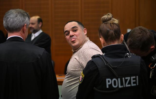 09 December 2025, Hesse, Frankfurt/Main: One of the three defendants, Ukrainian Robert A. (C), sticks out his tongue as he is led into the courtroom on the opening day of the trial against three men for spying for Russia. Three men are said to have had a man in their sights for a Russian secret service. A crucial meeting is said to have been planned in a cafe in Frankfurt. Now the trial begins. Photo: -/POOL/AFP/dpa