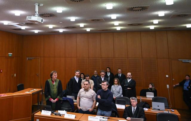 09 December 2025, Hesse, Frankfurt/Main: Ukrainian defendant Robert A. (front row, 2nd L) with his lawyer Daniel Beisel (front row, L), Armenian defendant Vardges I. (2nd row, 2nd L) and his lawyer Tobias Groscurth (2nd row, L) and Russian defendant Arman S. (back row, 2nd L) and his lawyer Andreas Bensch (back row, 2nd R), stand in the courtroom on the first day of the trial against three men for spying for Russia. Three men are said to have had a man in their sights for a Russian secret service. A crucial meeting is said to have been planned in a cafe in Frankfurt. Now the trial begins. Photo: -/POOL/AFP/dpa
