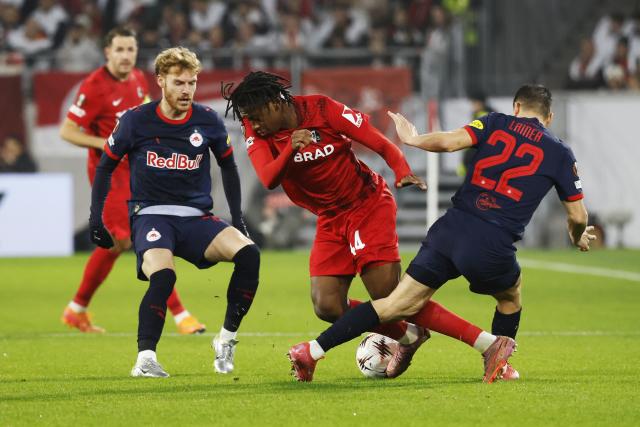 11 December 2025, Baden-Wuerttemberg, Freiburg im Breisgau: Freiburg's Johan Manzambi (C) battles for the ball with Salzburg's Stefan Lainer (R) and Yorbe Vertessen during the UEFA Europa League soccer match between SC Freiburg and RB Salzburg at Europa-Park Stadium. Photo: Philipp von Ditfurth/dpa