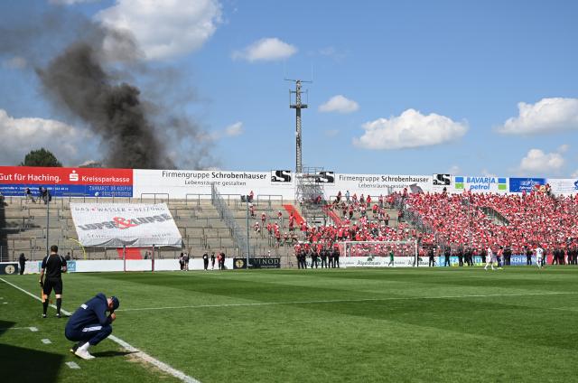 FILED - 11 June 2023, Bavaria, Unterhaching: Unterhaching coach Sandro Wagner (L) sits on the edge of the pitch while thick smoke rises behind the north stand during the the Regionalliga promotion round to the 3rd division soccer match between SpVgg Unterhaching and Energie Cottbus at Sportpark Unterhaching. The Bild paper said the council of the municipality of Unterhaching near Munich has given the green light to sell its 15,000-seat Sportpark Unterhaching stadium to Bayern for ·7.25 million ($8.5 million). Photo: Angelika Warmuth/dpa