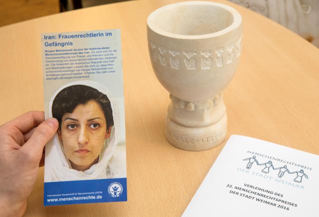 FILED - 10 December 2016, Thuringia, Weimar: A man holds a flyer with a picture of the laureate next to the award at a press conference on the sidelines of the Weimar Human Rights Award ceremony for Iranian activist Narges Mohammadi. Photo: -/dpa-Zentralbild/dpa