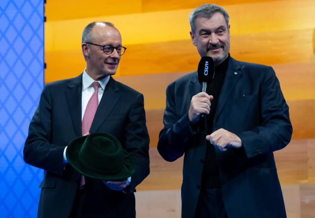 13 December 2025, Bavaria, Munich: Markus Soeder (r), CSU Chairman and Minister President of Bavaria, and German Chancellor Friedrich Merz, stand on stage at the CSU party conference in the exhibition hall. Merz holds a traditional hat in his hands, which he had previously received as a gift from the CSU. Photo: Sven Hoppe/dpa