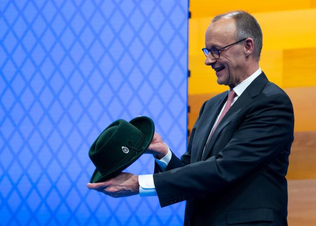 13 December 2025, Bavaria, Munich: German Chancellor Friedrich Merz  stands on stage at the CSU party conference in the exhibition hall. Merz holds a traditional hat in his hands, which he had previously received as a gift from the CSU. Photo: Sven Hoppe/dpa