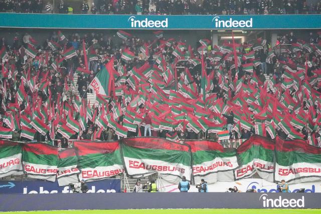 13 December 2025, Hesse, Frankfurt/M.: Augsburg fans cheer with scarves in the stands during the German Bundesliga soccer match between Eintracht Frankfurt and FC Augsburg at Deutsche Bank Park. Photo: Marc Schüler/dpa - WICHTIGER HINWEIS: Gemäß den Vorgaben der DFL Deutsche Fußball Liga bzw. des DFB Deutscher Fußball-Bund ist es untersagt, in dem Stadion und/oder vom Spiel angefertigte Fotoaufnahmen in Form von Sequenzbildern und/oder videoähnlichen Fotostrecken zu verwerten bzw. verwerten zu lassen.