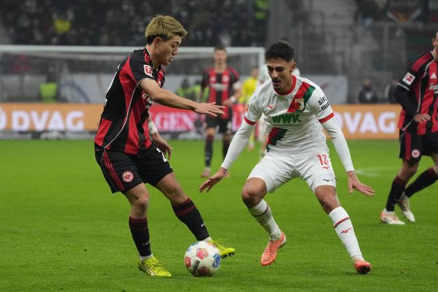 13 December 2025, Hesse, Frankfurt/M.: Augsburg's Dimitrios Giannoulis (R) and Eintracht Frankfurt's Ritsu Doan battle for the ball during the German Bundesliga soccer match between Eintracht Frankfurt and FC Augsburg at Deutsche Bank Park. Photo: Marc Schüler/dpa - WICHTIGER HINWEIS: Gemäß den Vorgaben der DFL Deutsche Fußball Liga bzw. des DFB Deutscher Fußball-Bund ist es untersagt, in dem Stadion und/oder vom Spiel angefertigte Fotoaufnahmen in Form von Sequenzbildern und/oder videoähnlichen Fotostrecken zu verwerten bzw. verwerten zu lassen.