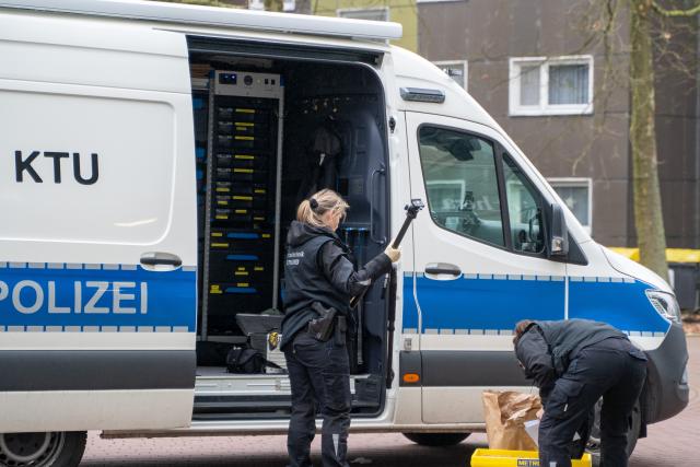 SCREENSHOT - 13 December 2025, North Rhine-Westphalia, Bergkamen: Policewomen stand at a police vehicle for the forensic investigation (KTU) at the scene, where a mother and her four children have been seriously injured in a knife attack in Bergkamen in the Ruhr region. Photo: Max Lametz/dpa