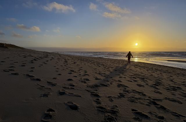 13 December 2025, Schleswig-Holstein, Rantum: A woman walks along the beach near Rantum on the North Sea island of Sylt in the light of the setting sun. Photo: Christian Charisius/dpa
