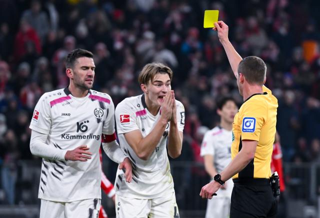 14 December 2025, Bavaria, Munich: Mainz's Kacper Potulski (C) receives a yellow card by referee Robin Braun during the German Bundesliga soccer match between Bayern Munich and FSV Mainz 05 at the Allianz Arena. Photo: Sven Hoppe/dpa - WICHTIGER HINWEIS: Gemäß den Vorgaben der DFL Deutsche Fußball Liga bzw. des DFB Deutscher Fußball-Bund ist es untersagt, in dem Stadion und/oder vom Spiel angefertigte Fotoaufnahmen in Form von Sequenzbildern und/oder videoähnlichen Fotostrecken zu verwerten bzw. verwerten zu lassen.