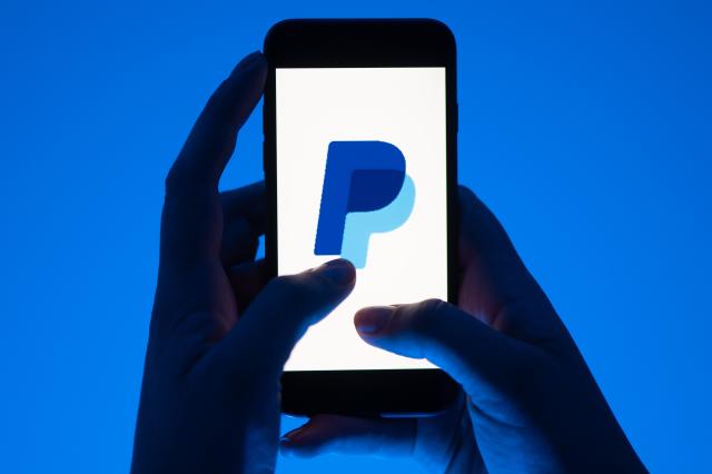 ILLUSTRATION - A woman holds a smartphone with the logo of the payment service Paypal. (posed scene)