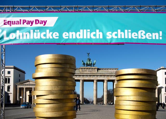 FILED - 07 March 2022, Berlin: Figures of coins pile up under a banner at an Equal Pay Day event in front of the Brandenburg Gate. Photo: Paul Zinken/dpa