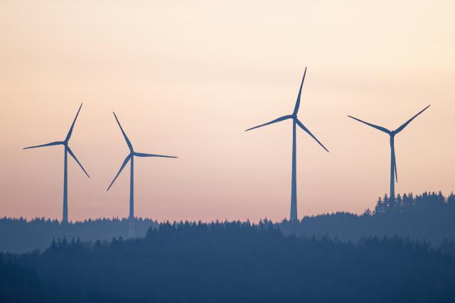 16 December 2025, Baden-Württemberg, Altenbach: Wind turbines stand in the light of the rising sun on a hill in the Odenwald. Photo: Uwe Anspach/dpa