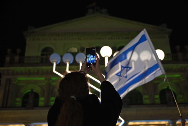 16 December 2025, Lower Saxony, Hanover: After a Hanukkah car parade, a person photographs an oversized Hanukkah menorah on Opera Square. Several vehicles traveled from Benjamin House to Opera Square for the celebration. Photo: Shireen Broszies/dpa