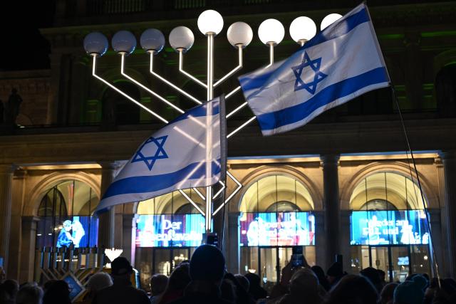 16 December 2025, Lower Saxony, Hanover: After a Hanukkah car parade, people gather in front of an oversized Hanukkah menorah on Opernplatz. Several vehicles traveled from Haus Benjamin to Opernplatz for the celebration. Photo: Shireen Broszies/dpa