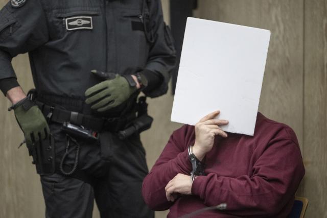 18 December 2025, Baden-Württemberg, Mannheim: The defendant (r) in a murder trial sits in a courtroom at Mannheim Regional Court and covers his face. According to the public prosecutor's office, the man deliberately drove towards people during a journey at the beginning of March. The public prosecutor's office sees no evidence of a political motive. Photo: Marijan Murat/dpa