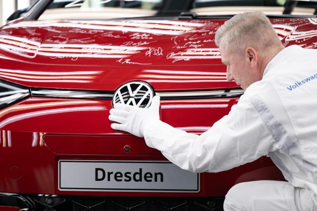 18 December 2025, Saxony, Dresden: In a staged scene, a VW employee kneels next to a red ID.3 in the light tunnel on the production line of Volkswagen's Transparent Factory, which has already been shut down. The vehicle was the last car to roll off the production line on December 16, 2025 and has been signed by all employees. Photo: Sebastian Kahnert/dpa