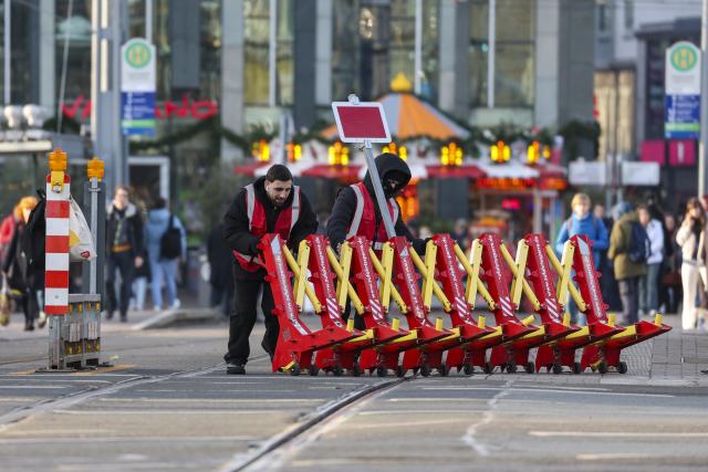 18 December 2025, Saxony, Leipzig: Two employees of a security company push a mobile barrier off the streetcar tracks at Augustusplatz. As part of the security measures for the Christmas market, these barriers always have to be opened and closed manually before the streetcars arrive and depart. Photo: Jan Woitas/dpa