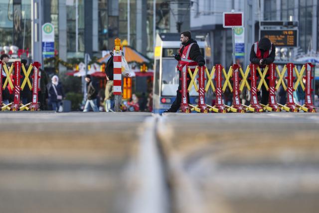 18 December 2025, Saxony, Leipzig: Two employees of a security company wait at a mobile barrier on the streetcar tracks at Augustusplatz. As part of the security measures for the Christmas market, these barriers always have to be opened and closed manually before the streetcars arrive and depart. Photo: Jan Woitas/dpa