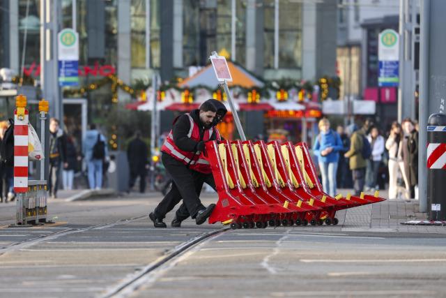 18 December 2025, Saxony, Leipzig: Two employees of a security company push a mobile barrier off the streetcar tracks at Augustusplatz. As part of the security measures for the Christmas market, these barriers always have to be opened and closed manually before the streetcars arrive and depart. Photo: Jan Woitas/dpa