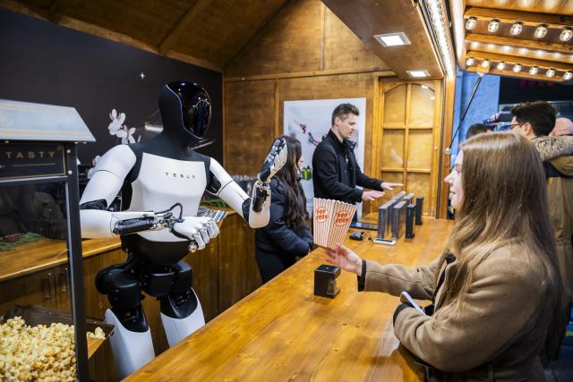 20 December 2025, Berlin: Tesla's humanoid robot 'Optimus' hands out popcorn to Lisa (R) during its presentation at the Mall of Berlin. Photo: Christoph Soeder/dpa