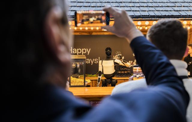 20 December 2025, Berlin: Tesla's humanoid robot 'Optimus' waves from a Christmas market stall while handing out popcorn during its presentation at the Mall of Berlin. Photo: Christoph Soeder/dpa