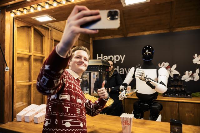 20 December 2025, Berlin: Tim takes a selfie with Tesla's humanoid robot 'Optimus' during its presentation at the Mall of Berlin. Photo: Christoph Soeder/dpa