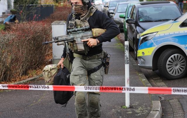 21 December 2025, North Rhine-Westphalia, Leverkusen: A heavily armed police officer holds a machine gun behind a police cordon during a police operation in Leverkusen. According to unconfirmed reports, there is an armed person in an apartment. Photo: Sascha Thelen/dpa