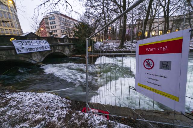 26 December 2025, Bavaria, Munich: A sign with the inscription "Warning! - No surfable wave! - Danger to life! - No surfing!" can be seen on a fence next to the Eisbach and the temporary Eisbach wave in the English Garden. The wave had not built up in the past two months. Since Christmas Day, surfers have been able to ride the standing wave again. The wave is normally a real hotspot for tourists and surfers from all over the world at any time of the year and day. Photo: Peter Kneffel/dpa