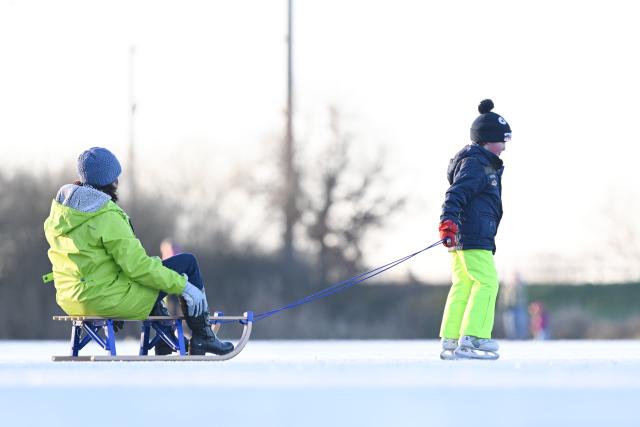 26 December 2025, Lower Saxony, Neermoor: A son pull her mother across the ice at the flooded surface in Neermoor lured on Boxing Day. Photo: Lars Penning/dpa