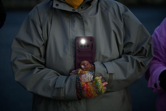 31 December 2025, Hamburg: A woman holds her cell phone with its flashlight switched on as part of a chain of lights around the Outer Alster under the motto "Hamburg togetHHer," calling for greater togetherness and against loneliness. Photo: Jonas Walzberg/dpa