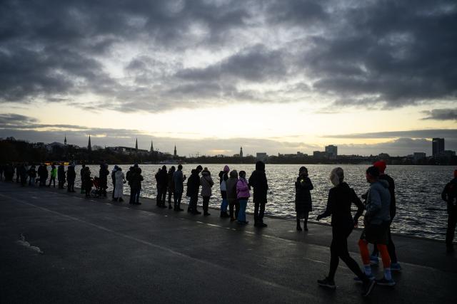 31 December 2025, Hamburg: Participants hold up their mobile phones with flashlights switched on during a chain of lights around the Outer Alster under the motto "Hamburg togetHHer," calling for solidarity and against loneliness. Photo: Jonas Walzberg/dpa