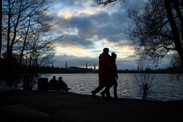 31 December 2025, Hamburg: Clouds drift above walkers along the Outer Alster in the early evening light at sunset. Photo: Jonas Walzberg/dpa