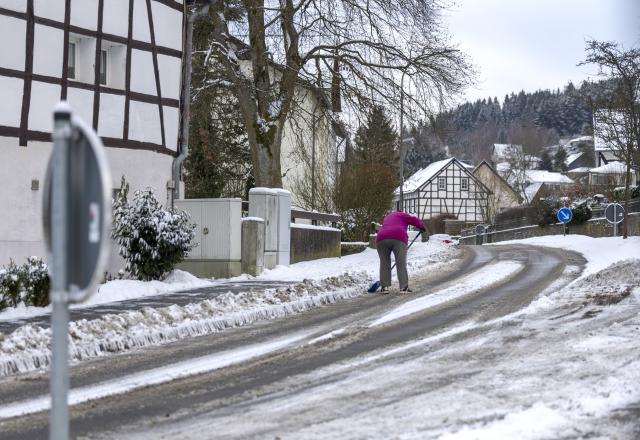 04 January 2026, North Rhine-Westphalia, Hellenthal: A woman clears the snow from in front of her house in the Eifel. Photo: Thomas Banneyer/dpa