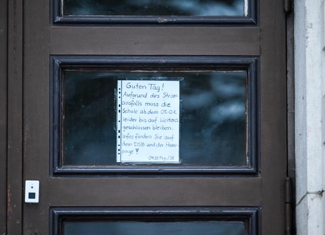 05 January 2026, Berlin: An information notice on the door of a grammar school reads "Hello, due to the power cut, the school must unfortunately remain closed from January 5 until further notice. Information can be found on the DSB and the homepage!".  Tens of thousands of people in the south-west of the capital have no electricity. Photo: Britta Pedersen/dpa