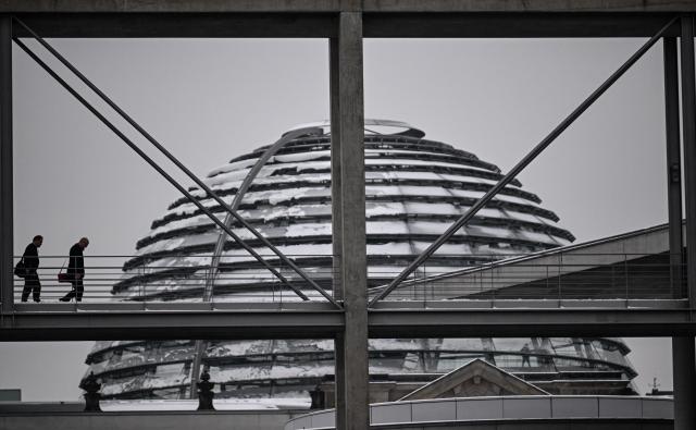 06 January 2026, Berlin: Two people walk across a bridge in front of the snow-covered dome of the Reichstag building in Berlin. Photo: Britta Pedersen/dpa