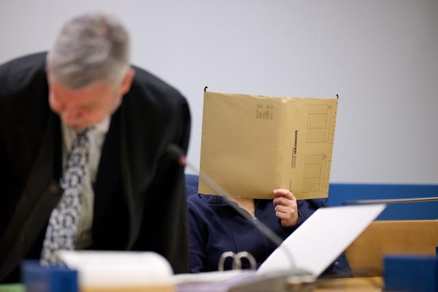 07 January 2026, North Rhine-Westphalia, Siegen: An accused mother hides her face behind a file in the courtroom. Lawyer Peter Endemann sits on the left. For seven years, from the time she was a baby, the woman is said to have kept her daughter in her grandparents' house in Attendorn in North Rhine-Westphalia - hidden away and completely isolated from the outside world. Photo: Bernd Thissen/dpa