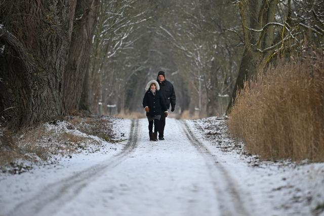 07 January 2026, Hesse, Moerfelden-Walldorf: Dagmar (L) and Uwe go for a walk on a snow-covered path in the Moenbruchweiher nature reserve. Photo: Michael Brandt/dpa