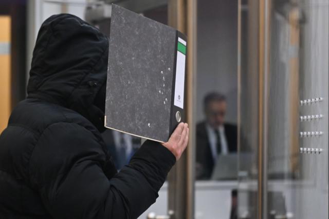 08 January 2026, North Rhine-Westphalia, Duesseldorf: The defendant holds a file folder in front of his face. A 33-year-old man from Monheim is on trial at the Higher Regional Court, accused of being a former Islamic State fighter and of terrorism, war crimes, crimes against humanity, and aiding and abetting murder. Photo: Federico Gambarini/dpa