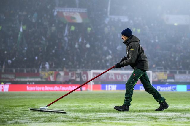 FILED - 03 December 2023, Bayern, Augsburg: A greenkeeper clears the snow off the during the halftime of the 2023 German Bundesliga soccer match between FC Augsburg and Eintracht Frankfurt at the WWK Arena. Photo: Tom Weller/dpa