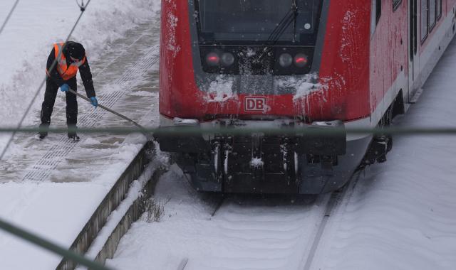 08 January 2026, Hamburg: A man removes a thick layer of snow from a platform at Hamburg Central Station. Photo: Marcus Brandt/dpa