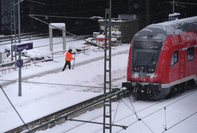 08 January 2026, Hamburg: A man removes a thick layer of snow from a platform at Hamburg Central Station. Photo: Marcus Brandt/dpa