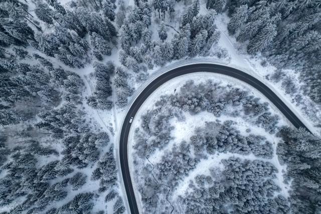 08 January 2026, Saxony, Klingenthal: An aerial view shows cars driving along a country road through the winter forest in Vogtland. Photo: Jan Woitas/dpa