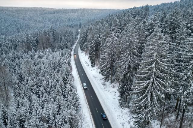 08 January 2026, Saxony, Klingenthal: An aerial view shows cars driving along a country road through the winter forest in Vogtland. Photo: Jan Woitas/dpa