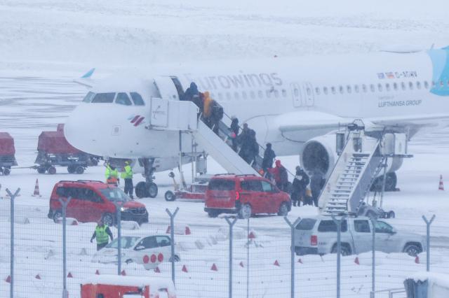 09 January 2026, Hamburg: Passengers board a Eurowings aircraft in snowy conditions and icy winds. Photo: Bodo Marks/dpa